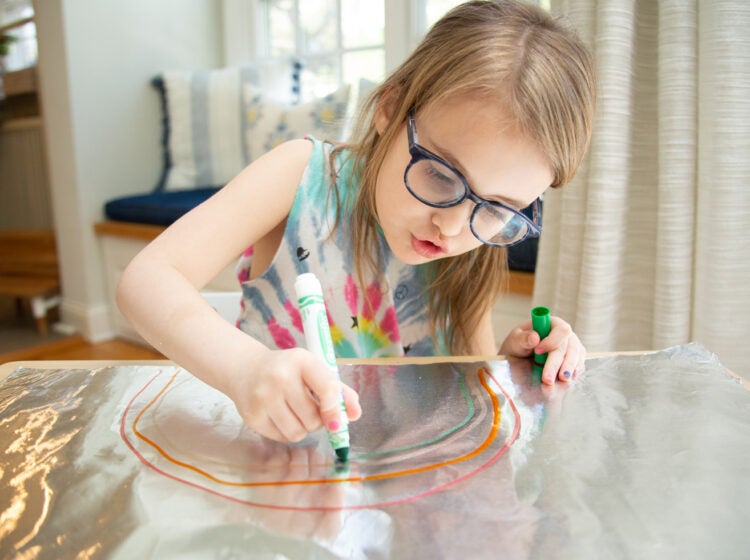 A child drawing a rainbow on tinfoil with magic markers.