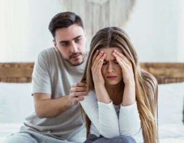 A woman distressed with her head in her hands while a man tries to console her.