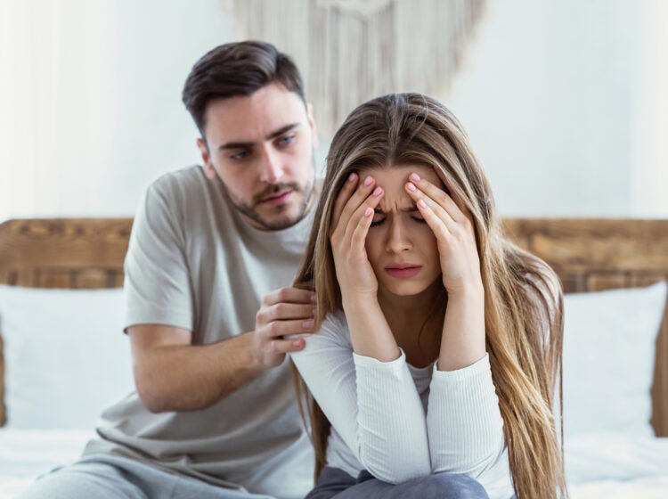 A woman distressed with her head in her hands while a man tries to console her.