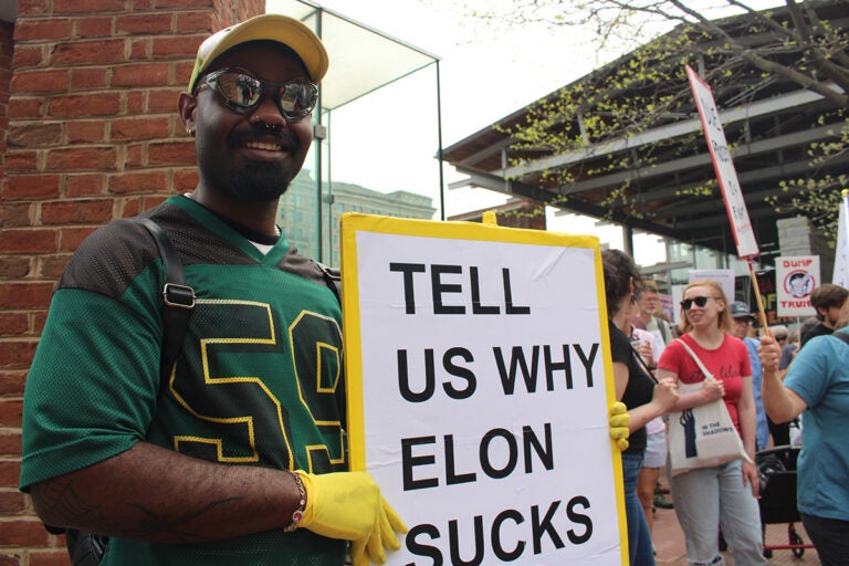 A man at a Philadelphia rally protesting the Trump administration holds up a sign reading 