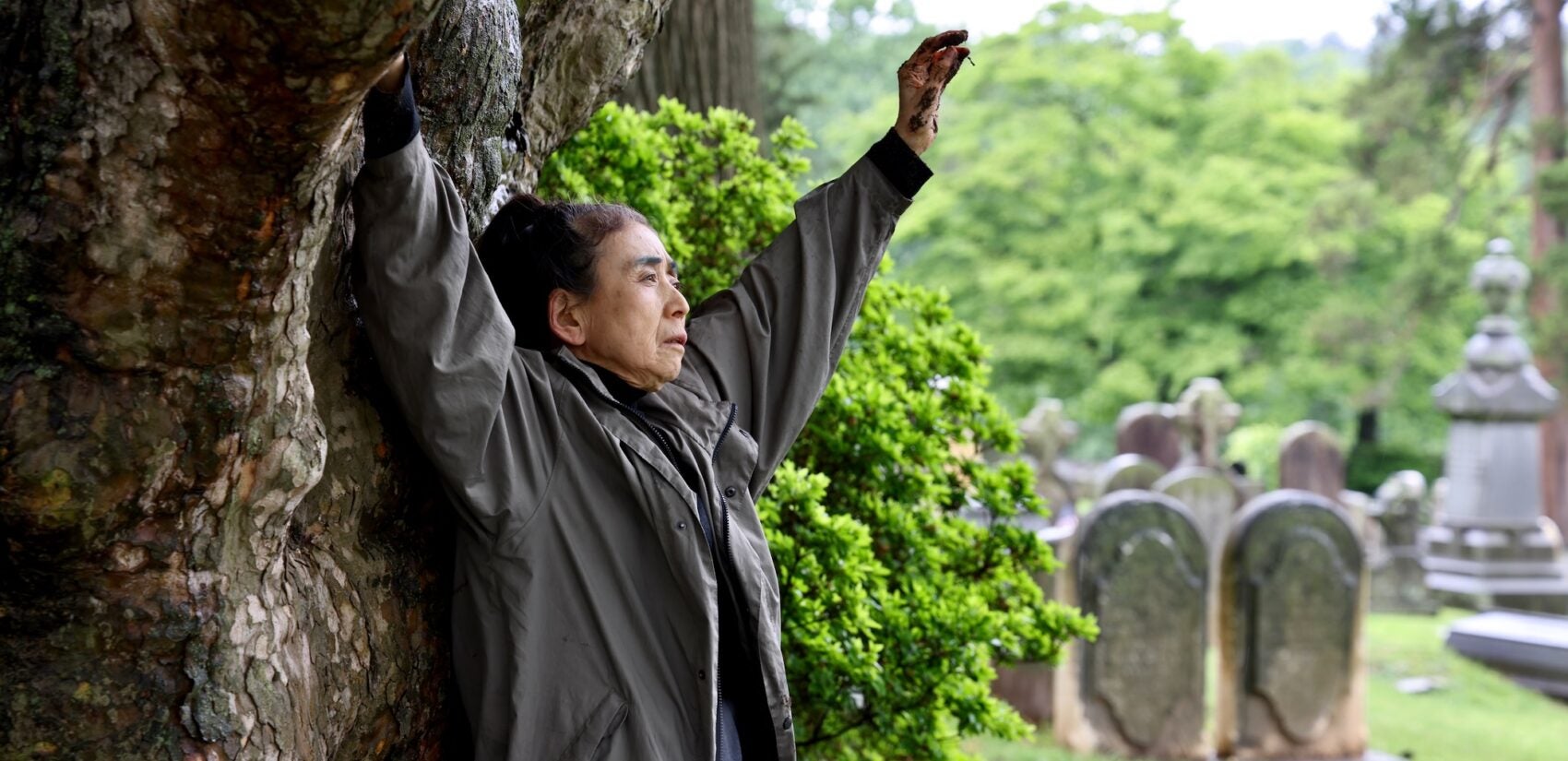 2025 05 28-e lee-eiko atake-philadelphia laurel hill cemetery-a body in places tree Eiko Otake raises her arms beneath a tree at Laurel Hill Cemetery for the Death and Arts Festival