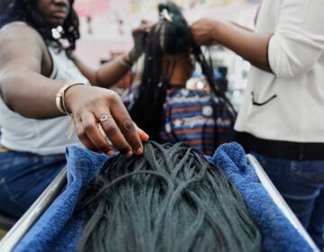 A braider picks up pieces of synthetic braiding hair