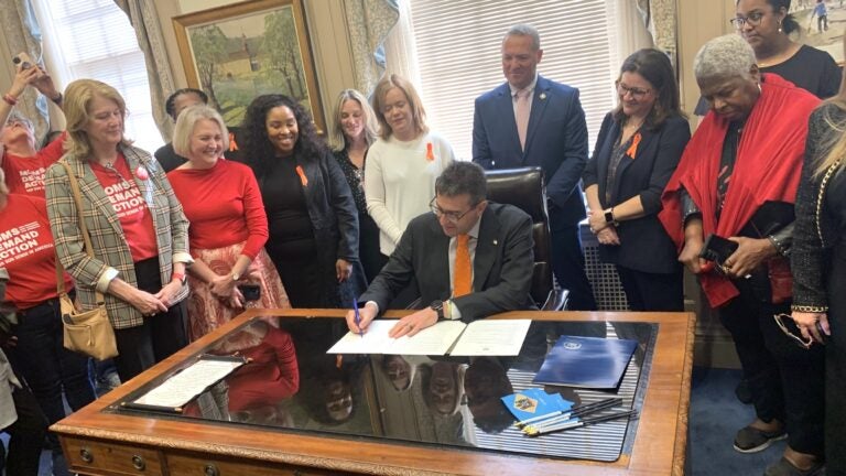 Meyer-Gun-violence-sign-s-mueller-2025-05-01 Matt Meyer signing a paper on his desk, surrounded by people