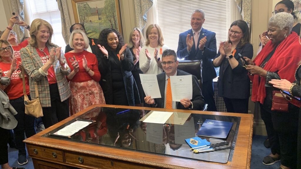 Matt Meyer signing a paper on his desk, surrounded by people