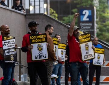 around 7 union members from the Brotherhood of Locomotive Engineers and Trainmen form a picket line, with signs reading LOCOMOTIVE ENGINEERS ON STRIKE