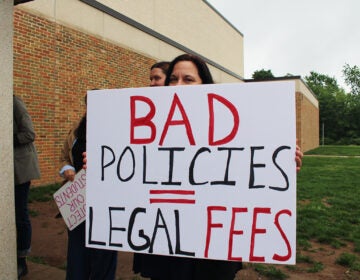 a parent protesting he possible appointment of Abram Lucabaugh as Centennial School District's new superintendent holds a sign reading BAD POLICIES = LEGAL FEES