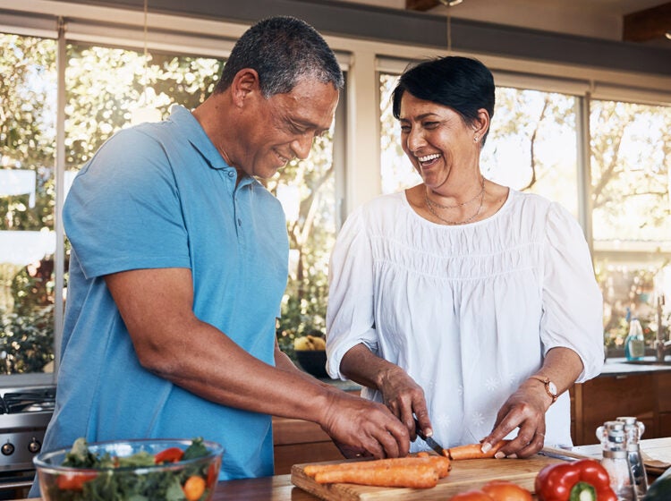 Mature, couple and healthy cooking in kitchen to chop vegetables for salad diet, nutrition and lunch meal at home. Happy man, woman and help cut carrot ingredients for love, care and support together