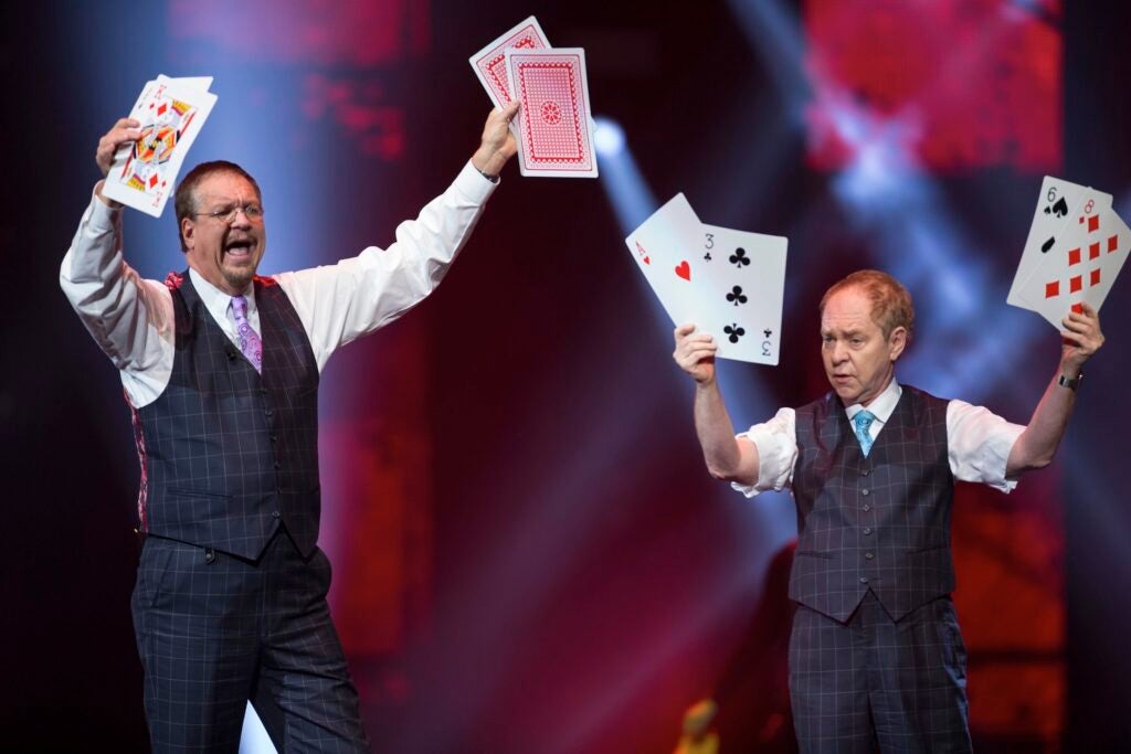 Penn and Teller on stage holding up oversized playing cards