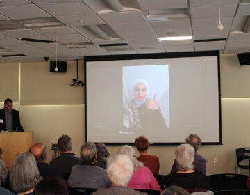 A woman from Northern Gaza is shown on a projector screen giving a thumbs up in front of a crowd