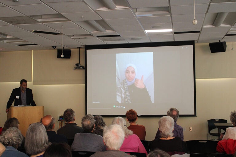 peoples-tribunal-1 A woman from Northern Gaza is shown on a projector screen giving a thumbs up in front of a crowd