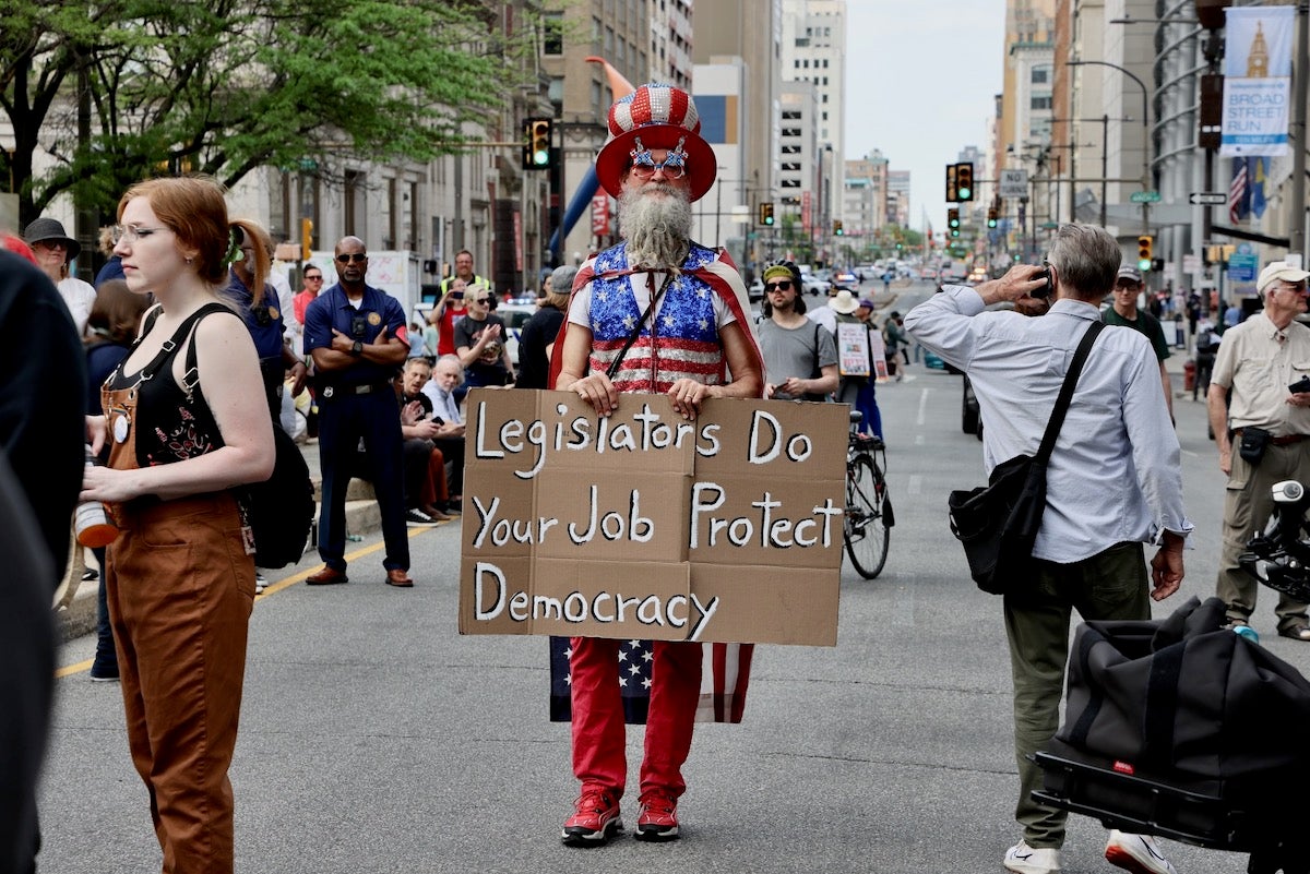2025 05 01-e lee-philadelphia city hall-may day rally with bernie flag man A man wearing an American flag carrying a sign during a May Day rally at Philadelphia City Hall