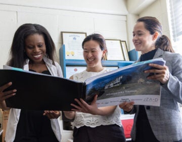 a HomeWorks Trenton dorm mom and two executives look at a book showing the future home of the organization