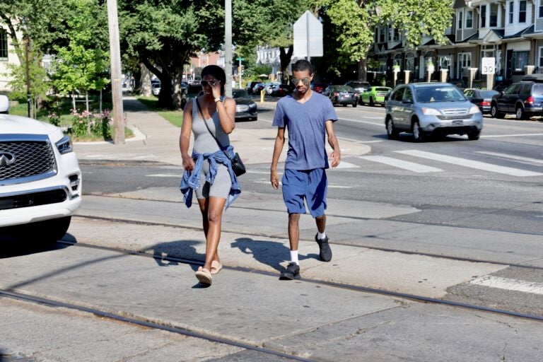 two people cross a crosswalk across Baltimore Avenue at Cobbs Creek Parkway