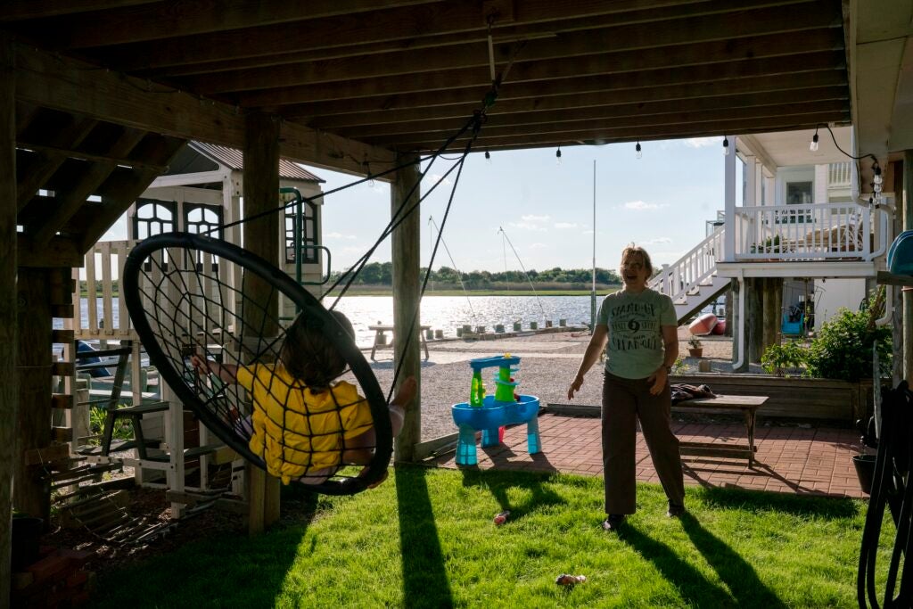 A woman pushing a child on a swing underneath a porch