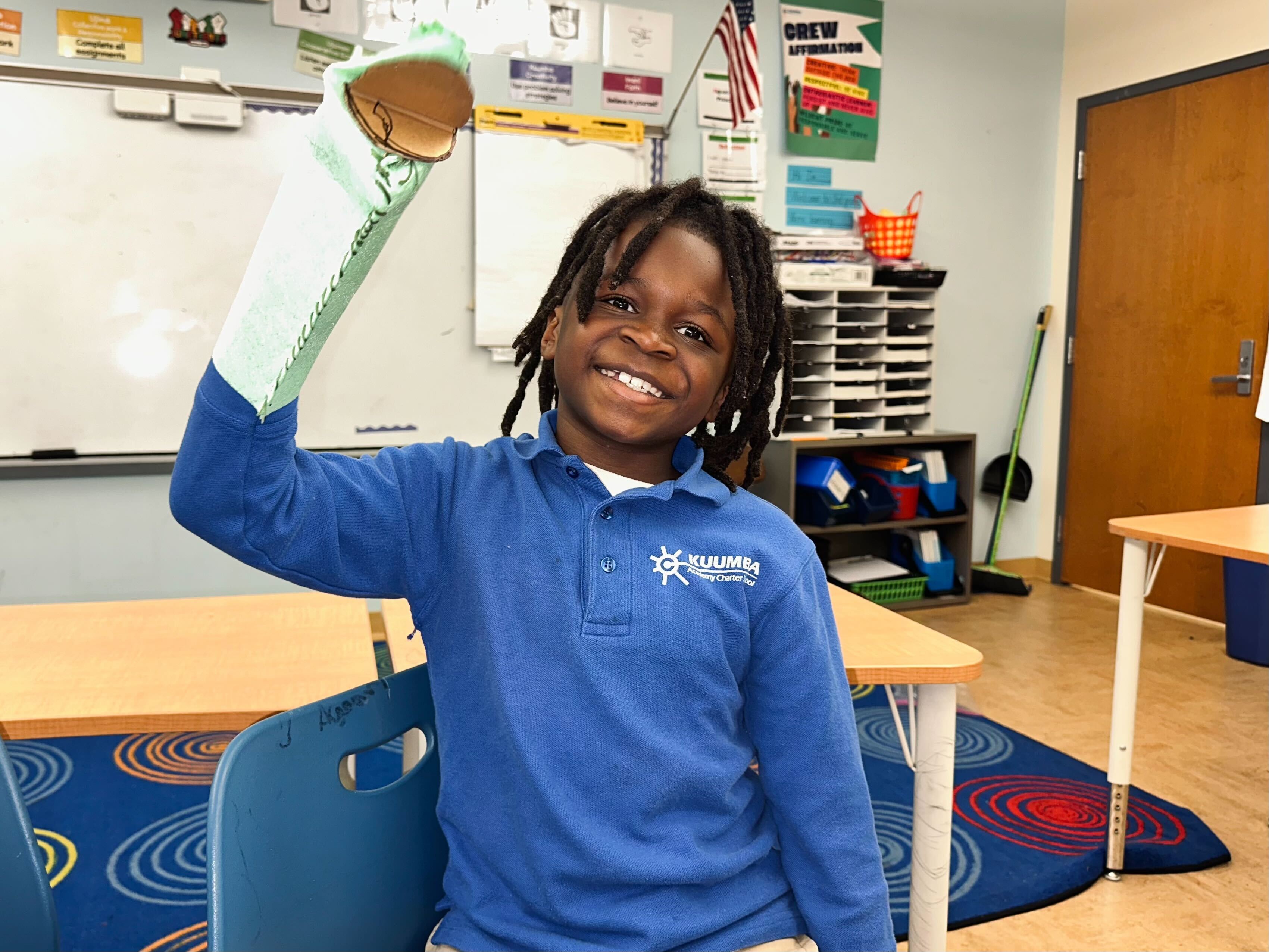 A third-grade student smiles with a puppet on a hand