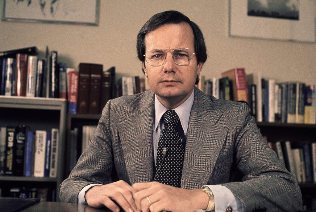 Archival photo of Bill Moyers posing for a photo at his desk