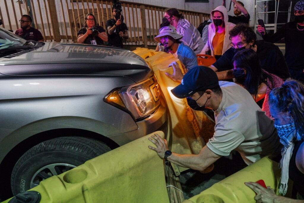 Protesters try to block a car from driving away