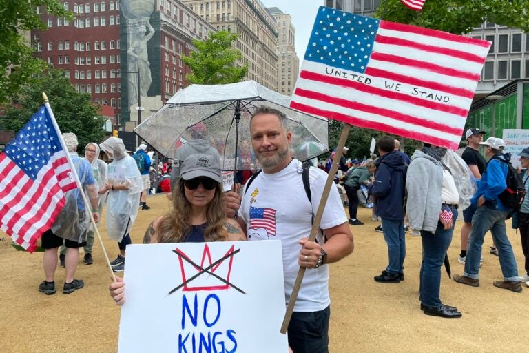 A man and a woman pose with American flags and signs protesting President Donald Trump