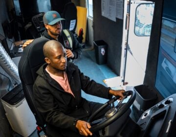 Trucking student Mohammed Kamal, left, overseen by instructor Tom Panton, practices driving a tractor-trailer truck in a simulation
