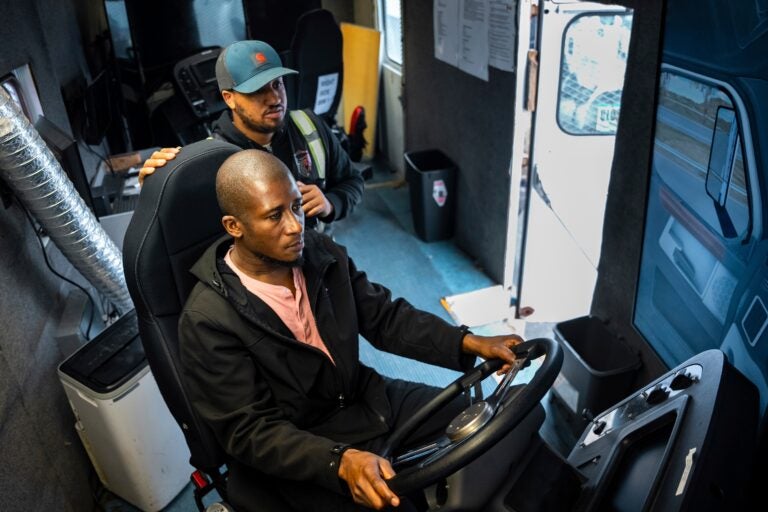 trucking-school-new-jersey Trucking student Mohammed Kamal, left, overseen by instructor Tom Panton, practices driving a tractor-trailer truck in a simulation
