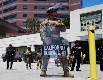 U.S. National Guard officers stand in full gear, with one officer carrying a riot shield, in Los Angeles