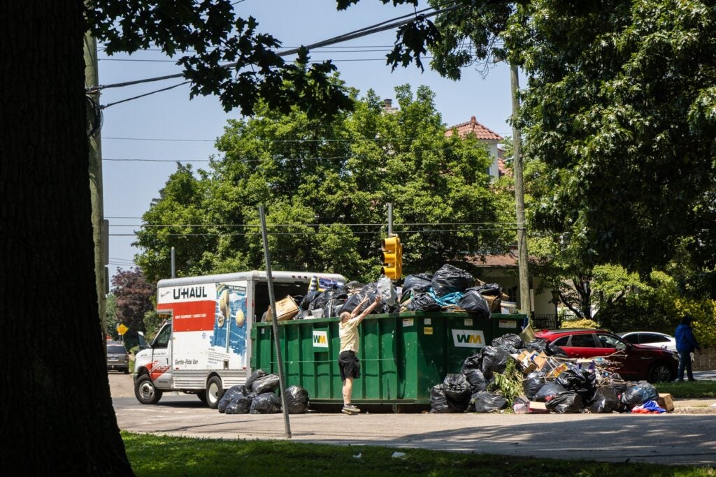 A resident struggles to add their trash bag to a dumpster