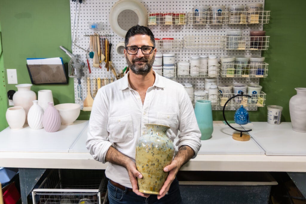 Artist and owner of Ahava Memorials Daniel Hoffman holds a ceramic vase in his shop