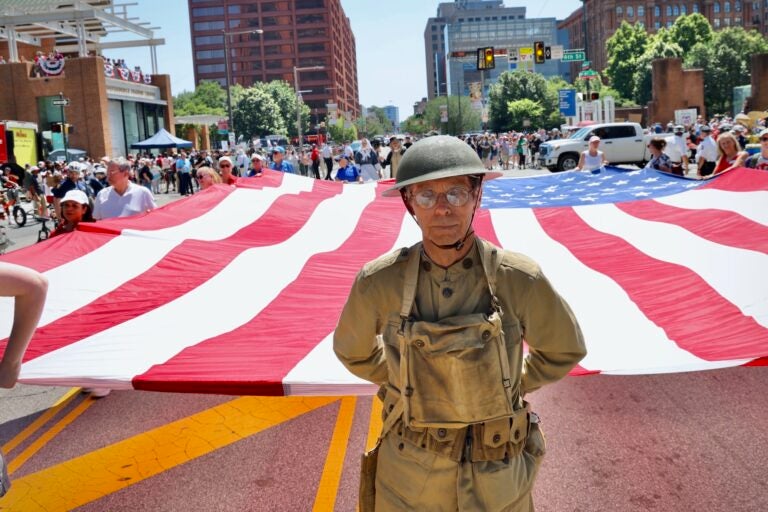 A man wearing an old military uniform helps hold a large American flag in Philadelphia.