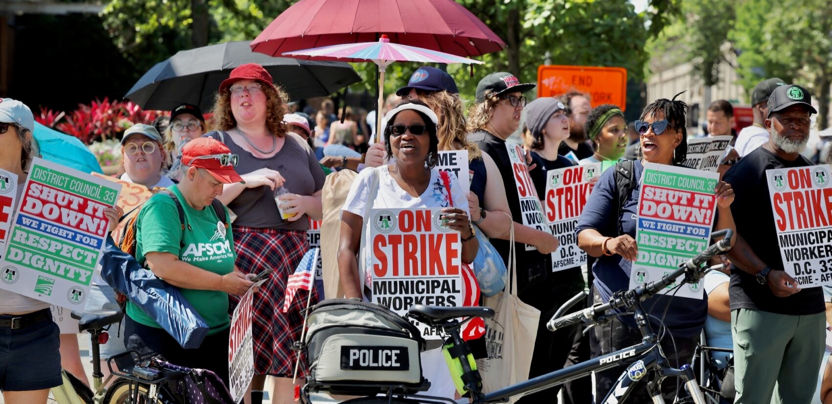 2025 07 04-e lee-philadelphia-4th of july parade strikers with umbrellas Striking Philadelphia municipal workers carry signs and chant during Philadelphia's Fourth of July parade.
