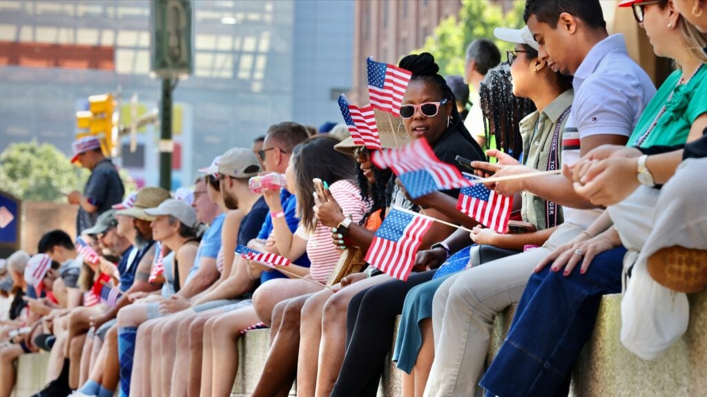 Spectators sit on a wall to watch Philadelphia's Fourth of July parade.