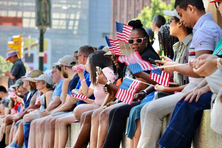 Spectators sit on a wall to watch Philadelphia's Fourth of July parade.