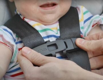 A close-up photo of an adult snapping a child into a car seat