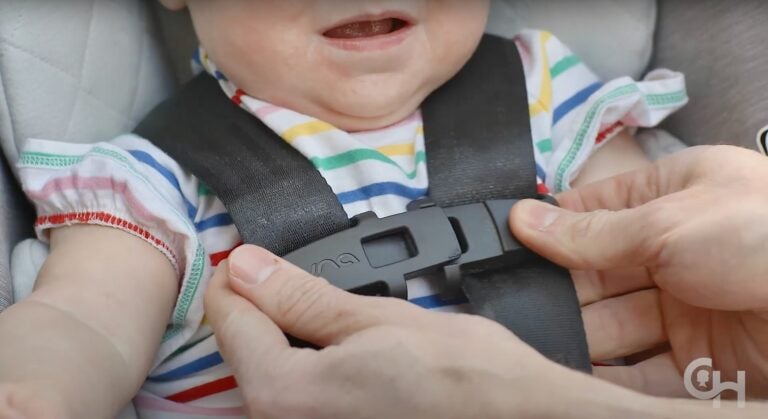 2025 07 23-provided-childrens hospital of pennsylvania car seat installation video harness clip A close-up photo of an adult snapping a child into a car seat