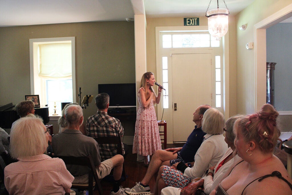 A woman sings in front of a seated audience inside a Doylestown home