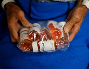 A person holds a plastic bag filled with prescription pill bottles. 