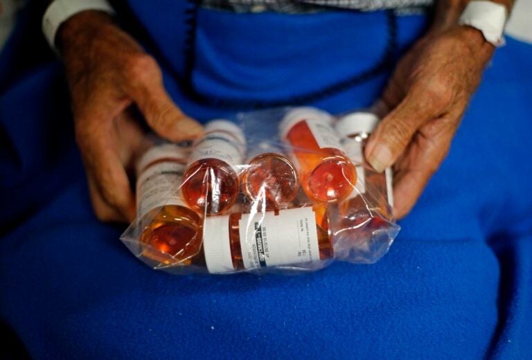 A person holds a plastic bag filled with prescription pill bottles. 
