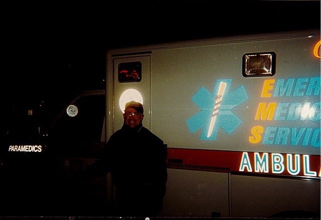 A man posing in front of an ambulance in the evening
