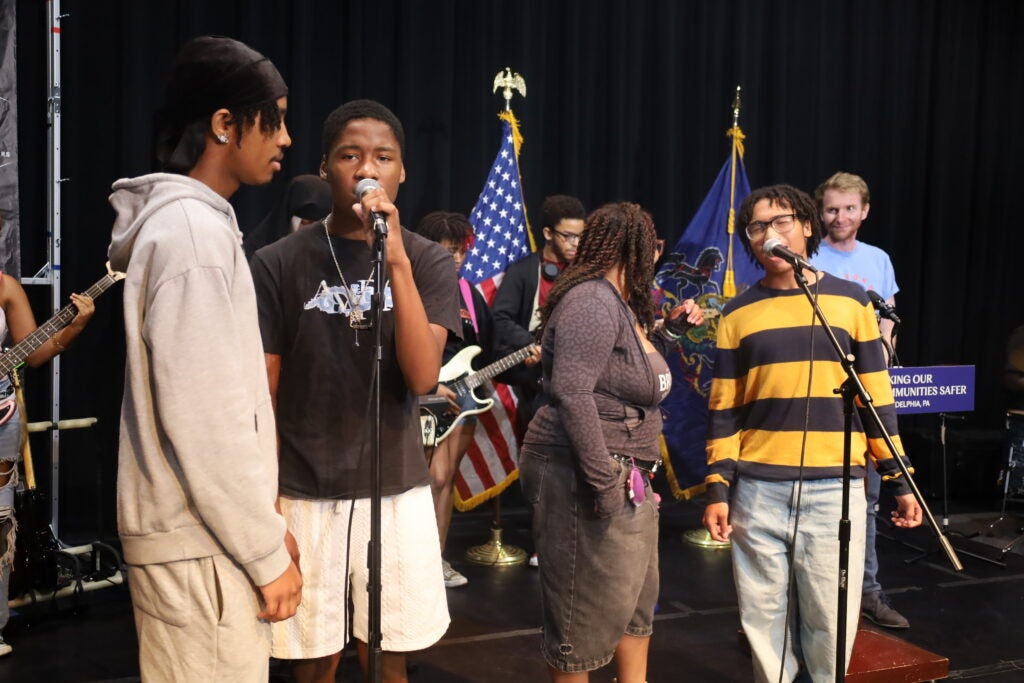 Students participating in the Beyond the Bars music program sing into microphones on a stage