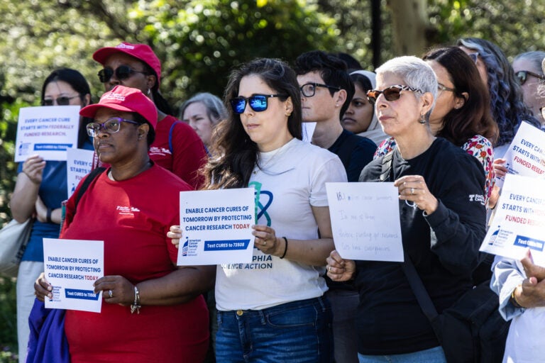 Researchers and cancer survivors hold signs at Independence Hall reading ENABLE CANCER CURES OF TOMORROW BY PROTECTING CANCER RESEARCH TODAY