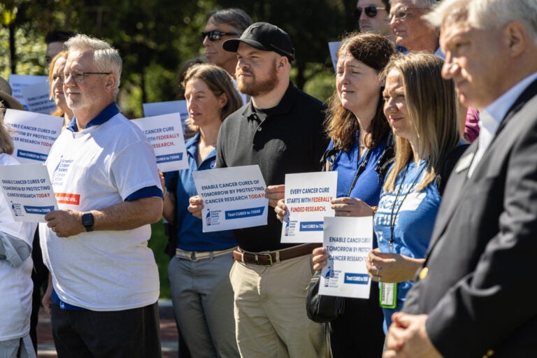 Researchers and cancer survivors hold signs at Independence Hall reading ENABLE CANCER CURES OF TOMORROW BY PROTECTING CANCER RESEARCH TODAY