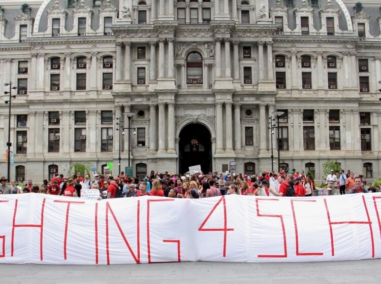 Teachers hold up a large sign in front of City Hall at the protest that reads 'FIGHTING 4 SCHOOLS'