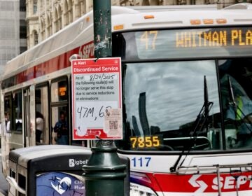 A bus pulls up to the curb, and a sign on a lightpole says that the line will be discontinued due to service reductions.