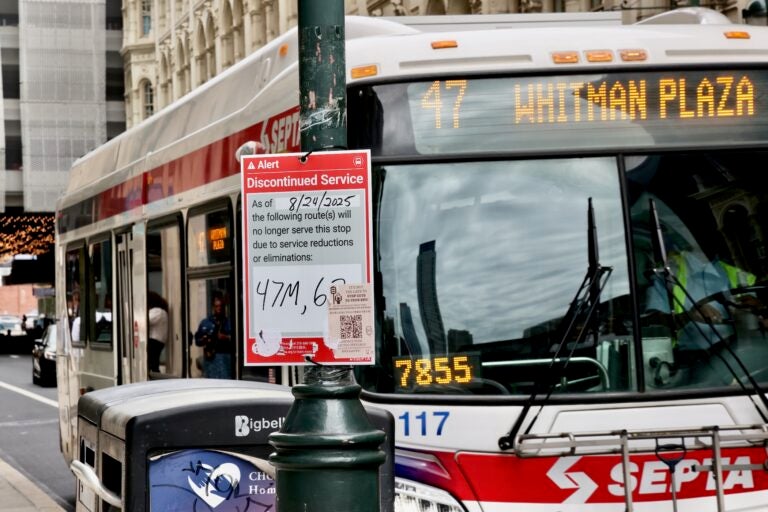 A bus pulls up to the curb, and a sign on a lightpole says that the line will be discontinued due to service reductions.
