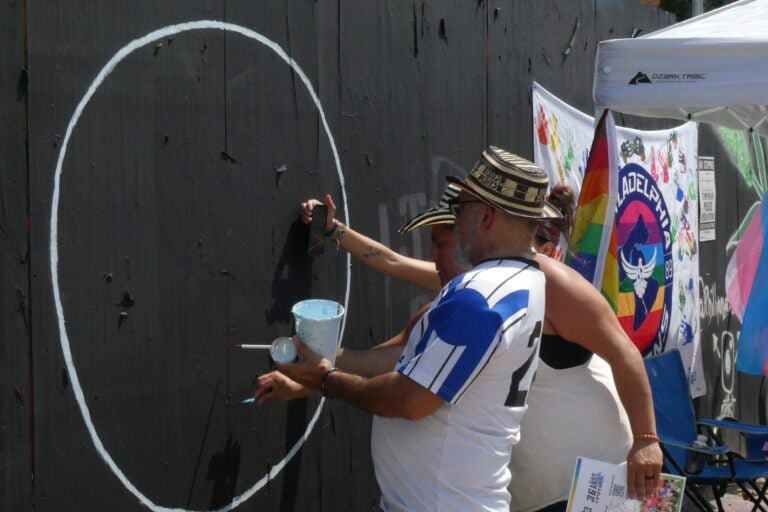 Two people chalk a wall with art