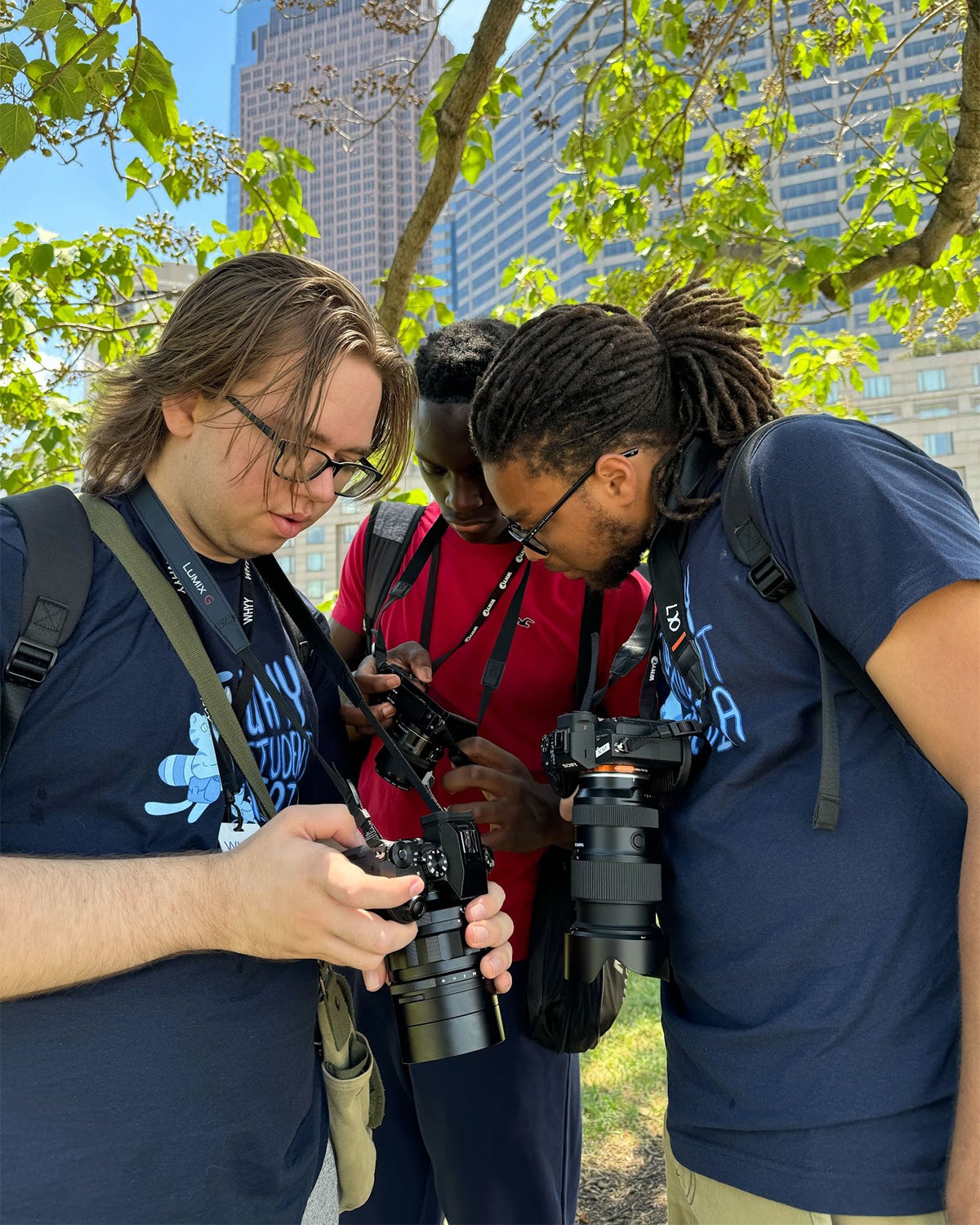 Three WHYY Media Labs students outside huddled over a camera