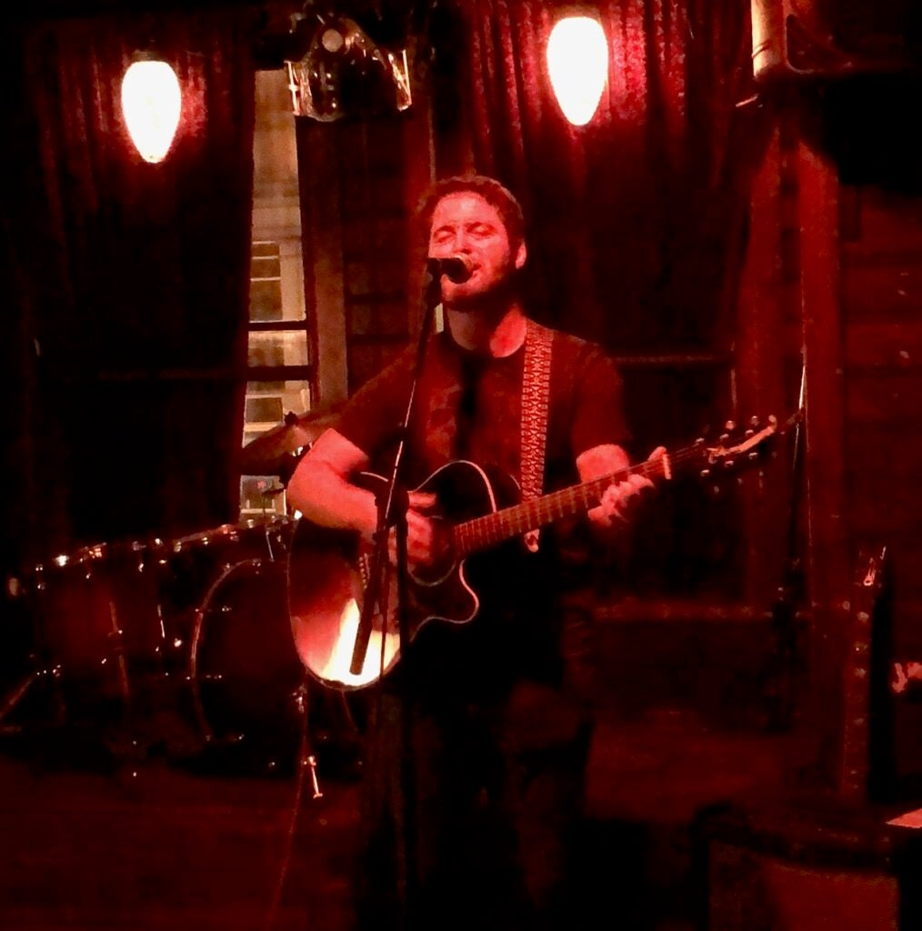 Adam Fishbein performing on stage with a guitar