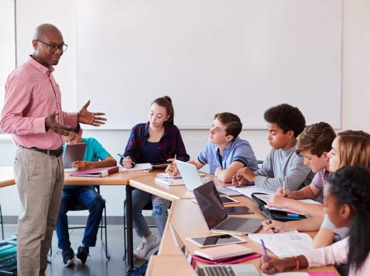 A high school teacher talking to students who are using technology in class. (Bigstock Image)