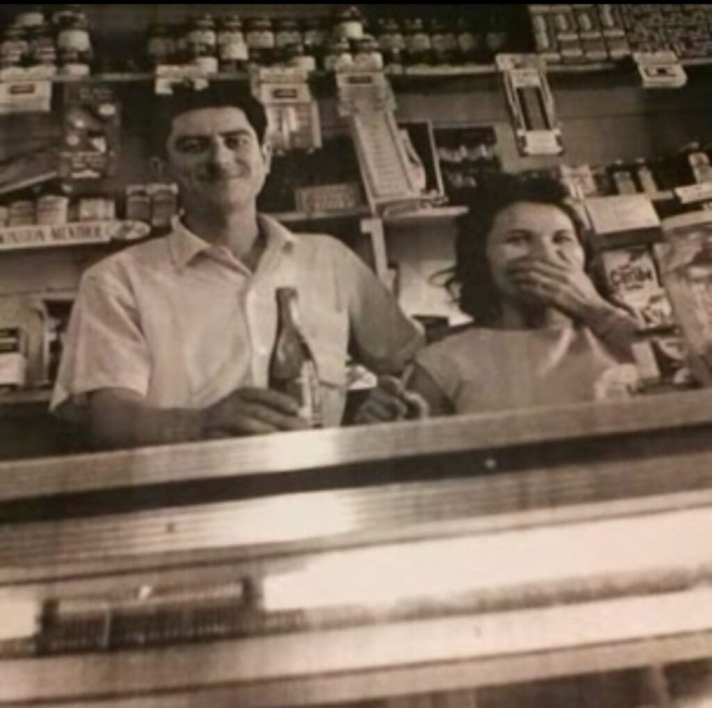 An archival photo of a man and woman posing for a photo while standing behind a counter at a store