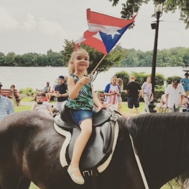 A young girl riding a horse and waving a Puerto Rican flag