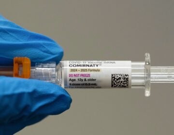 Someone wearing blue gloves holding a needle with a vaccine shot